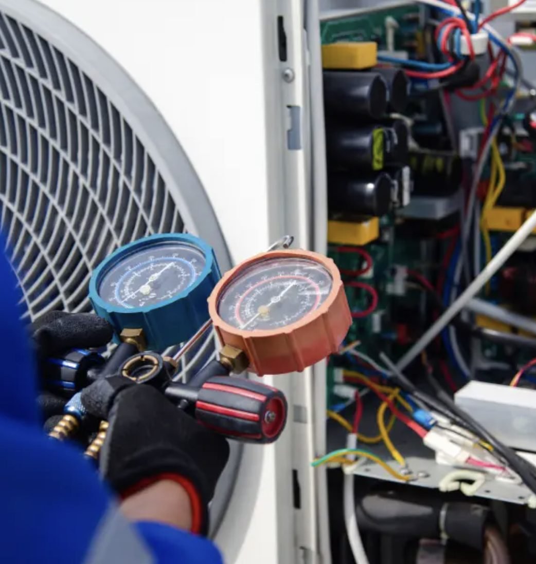 Engineer checking refrigerant pressures on an air conditioning outdoor unit with manifold gauges