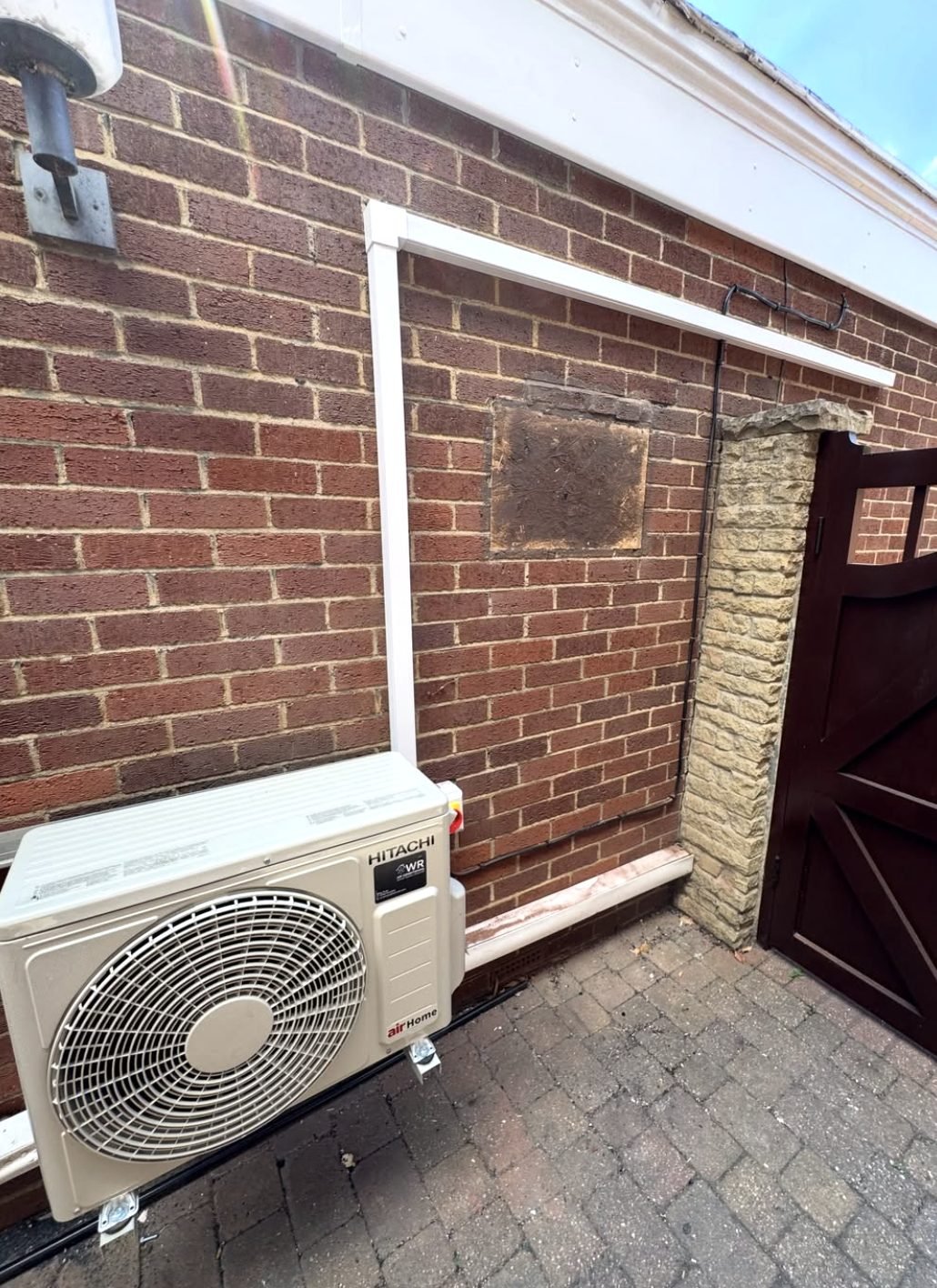 Hitachi airHome outdoor condenser unit on a brick wall with white boxed pipework